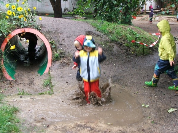 Kinder bei Regen im Garten beim Plantschen im Wasser